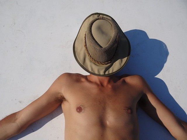 homme qui bronze au soleil, se protège avec un chapeau